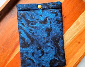 Puede incluir: Una bolsa de tela azul y negra con cierre de botón dorado. La tela tiene un patrón de mármol con motas doradas.