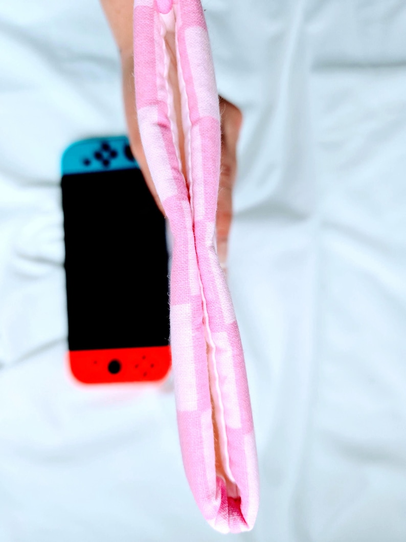 Puede incluir: Una bolsa de tela a cuadros rosa y blanca con forro blanco. La bolsa est&aacute; doblada por la mitad y sostenida por una mano.