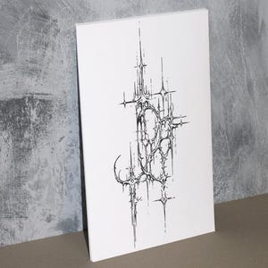Op de afbeelding: Een witte canvas print met een zwart, abstract ontwerp. Het kunstwerk heeft een complex, stekelig patroon met een gotische of architecturale esthetiek. De print leunt tegen een grijze muur.
