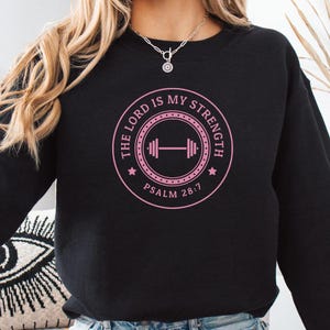 May include: Black sweatshirt with a pink graphic design that says "The Lord is my strength, Psalm 28:7" with a dumbbell icon.