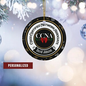 May include: A black and gold Christmas ornament with a white circle in the center. The circle has the text "Cisco Certified Network Associate" around the outside and "CCNA" in the center. The text "David Johnson" is below the CCNA logo. The ornament is personalized with the text "EST. 2024".