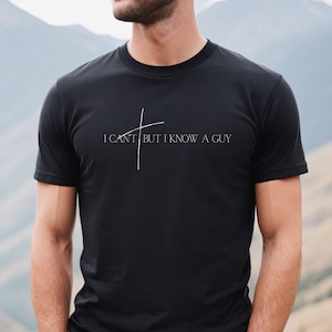 May include: Black t-shirt with a white graphic that says "I can't but I know a guy" with a stylized cross above the text.