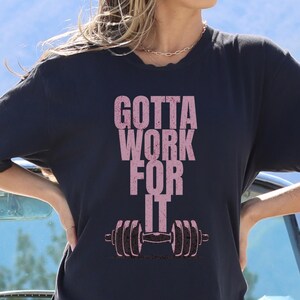 May include: A black t-shirt with the text "GOTTA WORK FOR IT" in pink lettering and a pink dumbbell graphic.
