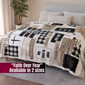 May include: A white fleece blanket with a patchwork design featuring black and white buffalo plaid, beige and brown text, and a cross. The text includes the phrases "Faith Over Fear", "My God is Able", "Trust God", "I am with you", "But God", "Do not fear", and "Psalm 34:4".
