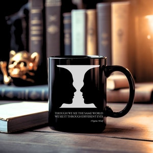 May include: Black coffee mug with a white silhouette of two faces that appear as one. The mug has the quote "Though we see the same world we see it through different eyes - Virginia Woolf" printed on the bottom.