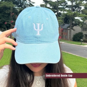 May include: A light blue denim baseball cap with a white embroidered Greek letter Psi.