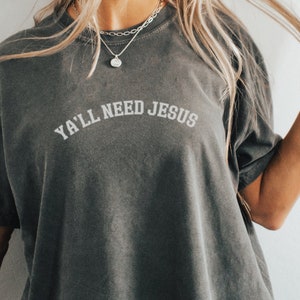 May include: A dark gray t-shirt with the text "Ya'll Need Jesus" in white lettering.