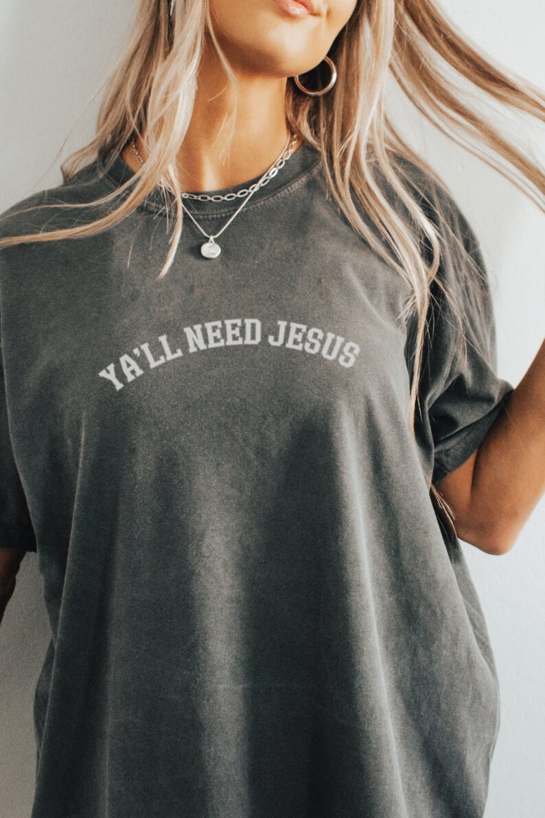 May include: A dark gray t-shirt with the text "Ya'll Need Jesus" in white lettering.