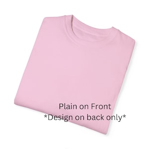 Może przedstawiać: Złożona, jasnor&oacute;żowa koszulka z okrągłym dekoltem. Prz&oacute;d koszulki jest gładki, z tekstem "Plain on Front *Design on back only*" wydrukowanym w prawym dolnym rogu.