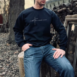 May include: A black sweatshirt with a white cross and the text "I can't but I know a guy" printed on the front.