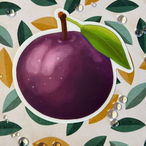 Puede incluir: Una pegatina de una ciruela morada con una hoja verde sobre un fondo blanco con un patrón de hojas verdes y amarillas.