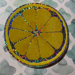 May include: A yellow lemon slice with a glittery iridescent border. The lemon slice is a sticker.