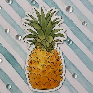 May include: A sticker of a yellow and orange pineapple with green leaves. The pineapple is on a white background with blue stripes and clear water droplets.