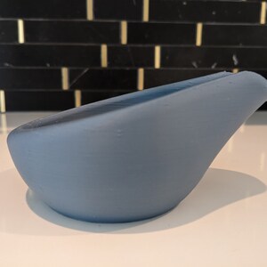 May include: A light blue, curved object with a smooth surface. The object has a rounded base and a slightly raised edge on one side. The item is likely a decorative piece or a small container.