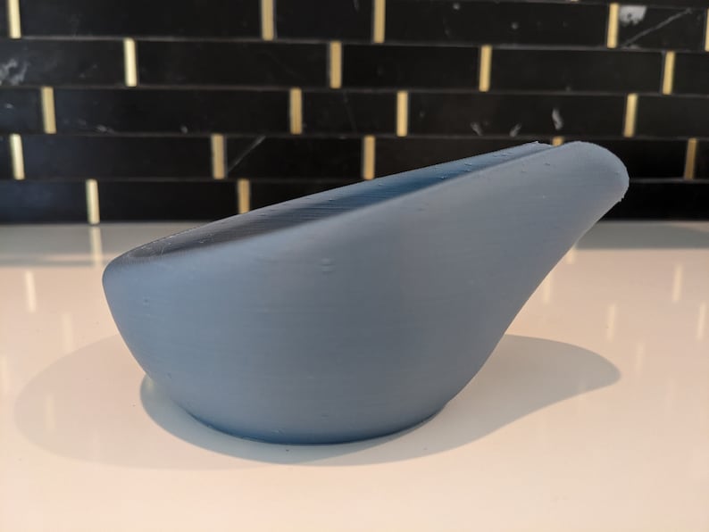 May include: A light blue, curved object with a smooth surface. The object has a rounded base and a slightly raised edge on one side. The item is likely a decorative piece or a small container.