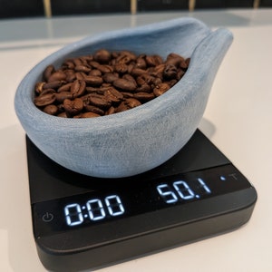 May include: A light blue, textured ceramic scoop filled with roasted coffee beans, resting on a black digital scale. The scale displays a weight of 1422 grams.