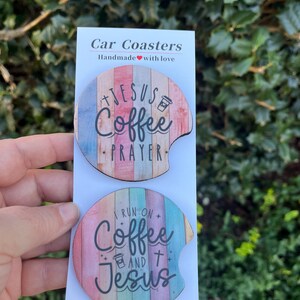 May include: Two round car coasters with a wood grain design. The top coaster features the text "Jesus Coffee Prayer" in black lettering. The bottom coaster features the text "I run on Coffee and Jesus" in black lettering.