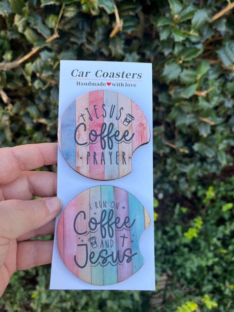 May include: Two round car coasters with a wood grain design. The top coaster features the text "Jesus Coffee Prayer" in black lettering. The bottom coaster features the text "I run on Coffee and Jesus" in black lettering.