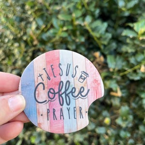 May include: A round, colorful coaster with a woodgrain pattern. It features the text "Jesus Coffee Prayer" and a small coffee cup icon.