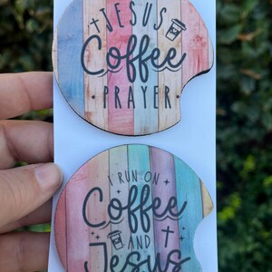 May include: Two round, colorful, wooden coasters with a white background. The top coaster has the text "Jesus Coffee Prayer" with a coffee cup icon. The bottom coaster has the text "I run on Coffee and Jesus" with a coffee cup icon and a cross.