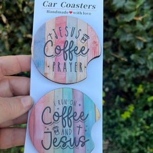 May include: Two round car coasters with a wood grain design. The top coaster features the text "Jesus Coffee Prayer" with a coffee cup icon. The bottom coaster features the text "I run on Coffee and Jesus" with a coffee cup icon and a cross.