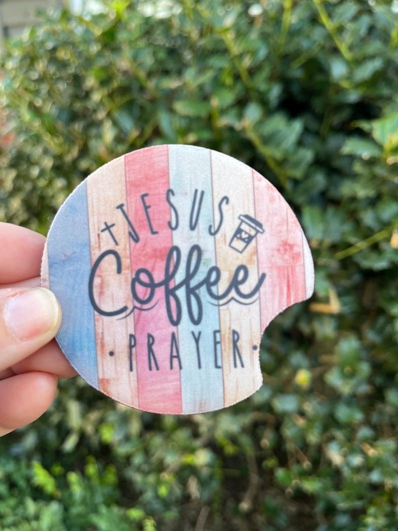 May include: A round, colorful coaster with a wood grain pattern. It features the text "Jesus Coffee Prayer" and a small coffee cup icon.