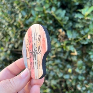 May include: A round wooden coaster with a distressed woodgrain design. The coaster features the text "Jesus + Coffee = Prayer" in black lettering with a coffee cup icon.