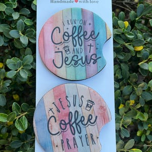 May include: Two round car coasters with a wood grain design. The top coaster has the text "I run on coffee and Jesus" with a coffee cup icon. The bottom coaster has the text "Jesus Coffee Prayer" with a coffee cup icon.