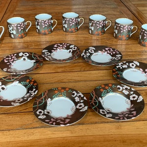 May include: Set of ten porcelain teacups and saucers with a floral pattern in shades of brown, pink, and orange. The cups and saucers have a gold rim.