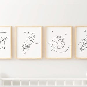 May include: Set of four black and white line art prints featuring space-themed illustrations. The prints depict a rocket, a planet, a ringed planet, and an astronaut.