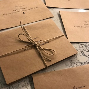 May include: A stack of brown paper envelopes tied with twine. Each envelope has the text "Open When..." followed by a special occasion, such as "It's our first Christmas as Mr. & Mrs." or "It's our wedding day."
