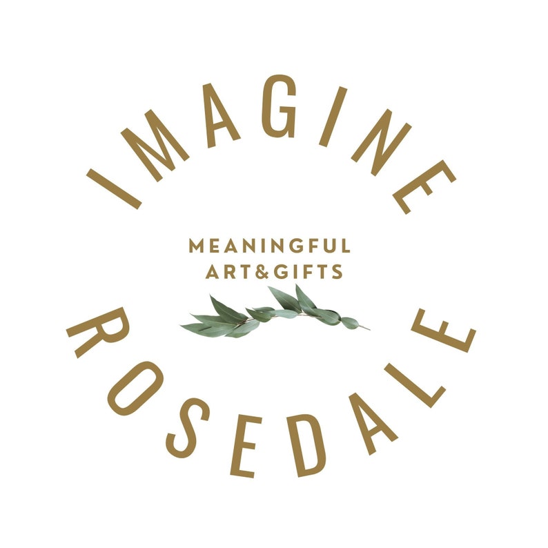 May include: Gold text on a white background reads "Imagine Rosedale" in a circular shape. The text "Meaningful Art & Gifts" is centred below the circle. A sprig of green eucalyptus leaves is centred below the text.