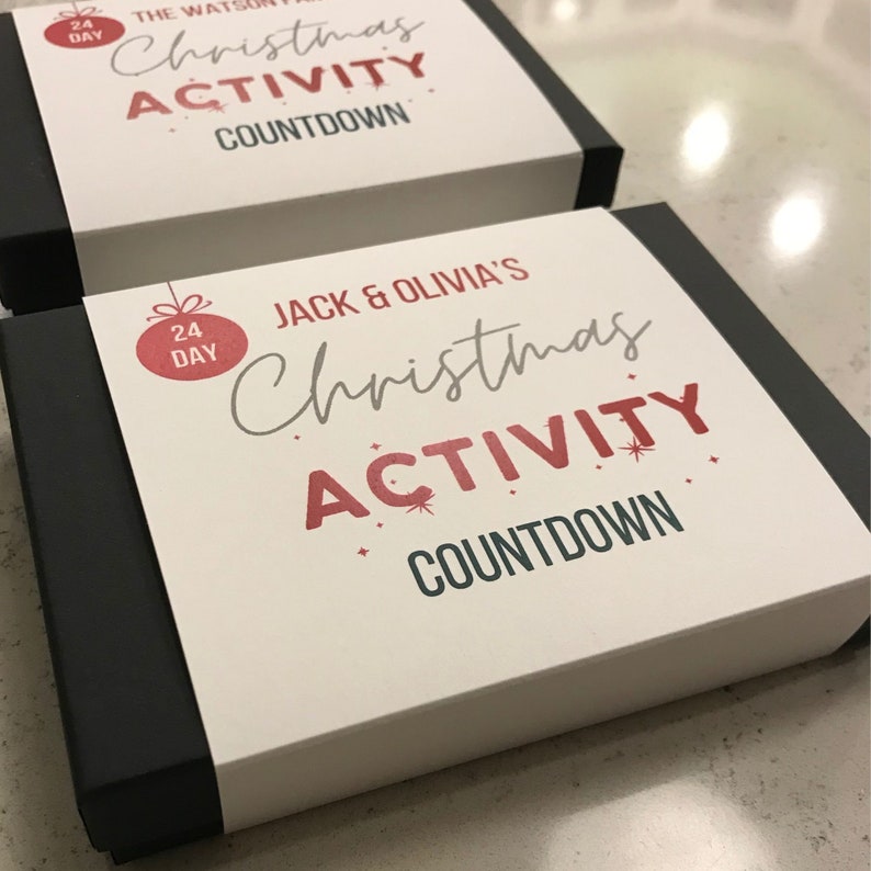 Puede incluir: Una caja blanca con ribete negro y un adorno navide&ntilde;o rojo y blanco. La caja tiene el texto "Jack & Olivia's Christmas Activity Countdown" impreso en ella.