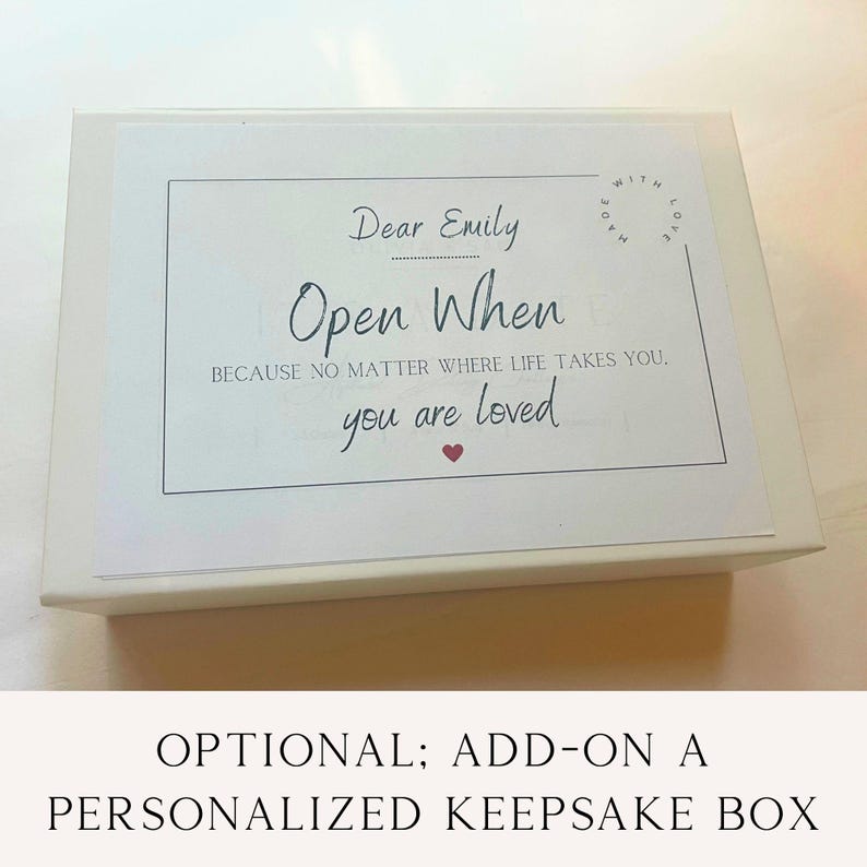 K&ouml;nnte beinhalten: Eine wei&szlig;e, rechteckige Erinnerungsbox mit einem Etikett, das den Text Dear Emily Open When BECAUSE NO MATTER WHERE LIFE TAKES YOU. you are loved, ein kleines rotes Herzsymbol und einen runden Stempel MADE WITH LOVE in der Ecke enth&auml;lt.