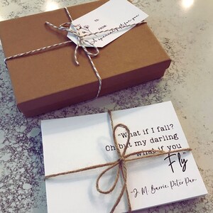 May include: A white card with a quote from J.M. Barrie's Peter Pan: "What if I fall? Oh but my darling what if you Fly". The card is tied with twine and placed on top of a brown gift box with a tag that reads "A special gift for you".