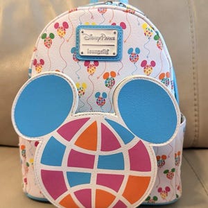 May include: White Loungefly backpack with a Disney Parks logo and Mickey Mouse balloon pattern. The front features a large Mickey Mouse head with a colorful globe design. The backpack has blue accents and a top handle.