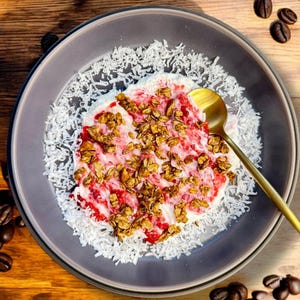 May include: A close-up of a bowl of yogurt with granola, strawberries, and shredded coconut. The bowl is on a wooden surface.
