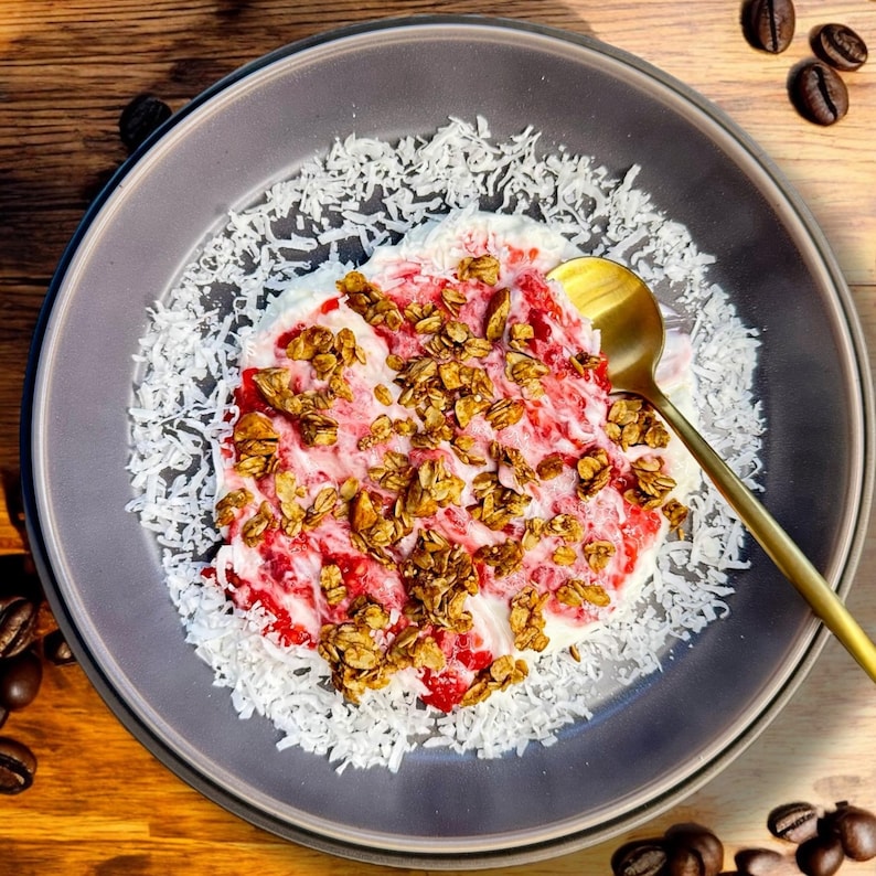 May include: A close-up of a bowl of yogurt with granola, strawberries, and shredded coconut. The bowl is on a wooden surface.