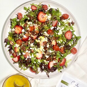 K&ouml;nnte beinhalten: Ein Salat mit verschiedenen Salaten, Erdbeeren, Tomaten, Feta-K&auml;se und Mandeln. Der Salat befindet sich auf einem wei&szlig;en Teller mit wei&szlig;em Hintergrund.