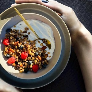 May include: A bowl of granola with yogurt, blueberries, and raspberries. The granola is topped with almonds and a golden spoon is resting on the side of the bowl.