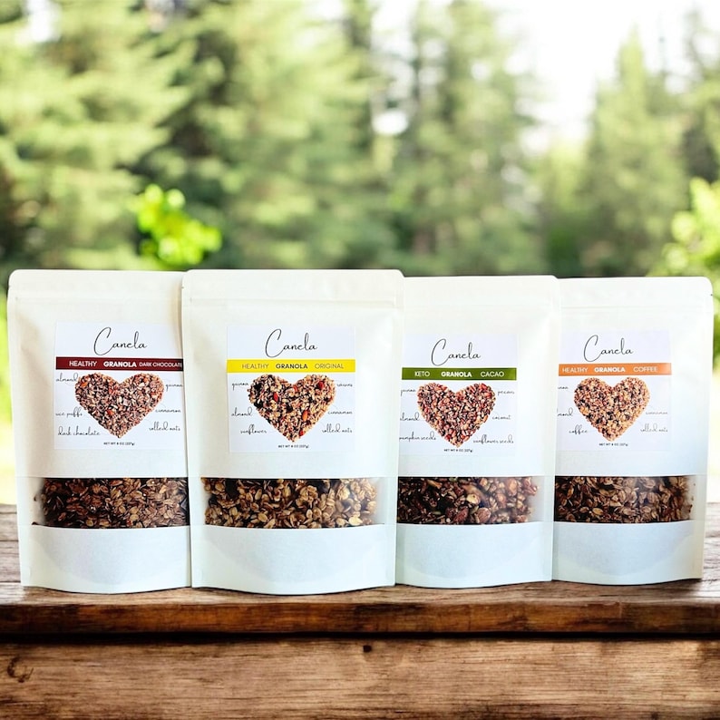 May include: Four white bags of granola with different flavours: Dark Chocolate, Original, Cacao, and Cookie. Each bag has a heart-shaped logo with the brand name "Canela" and a list of ingredients.