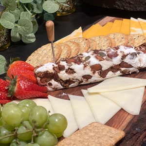 K&ouml;nnte beinhalten: Ein Holzbrett mit einer Auswahl an Snacks, darunter ein K&auml;selog mit Mandeln und Samen, Cracker, Erdbeeren, Trauben und K&auml;sescheiben.