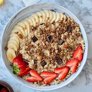 Puede incluir: Un cuenco de avena con rodajas de pl&aacute;tano, fresas, granola, almendras y trozos de chocolate. El cuenco tiene un dise&ntilde;o de m&aacute;rmol azul y blanco. Un desayuno o merienda saludable.