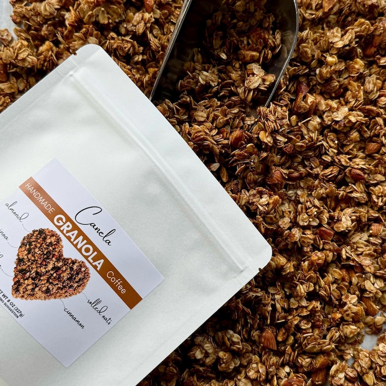 May include: A white resealable bag filled with granola. The bag has a label that reads "Handmade Cancla Granola Coffee" with a heart-shaped graphic of the granola. The label also lists the ingredients: "almond, cinnamon, rolled oats".