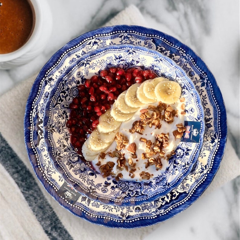 May include: A blue and white patterned bowl filled with yogurt, granola, sliced bananas, and pomegranate seeds.