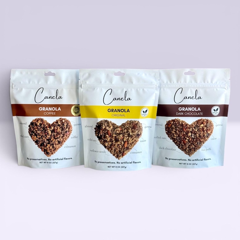 Puede incluir: Tres bolsas blancas de granola "Canela", cada una con un dise&ntilde;o de granola en forma de coraz&oacute;n. Los sabores son Caf&eacute;, Original y Chocolate Negro. Las bolsas indican "Sin conservantes. Sin sabores artificiales."