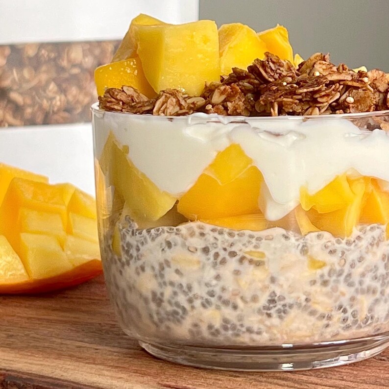 May include: A glass jar filled with layers of chia pudding, mango, yogurt, and granola. The mango is diced and the granola is a light brown colour.
