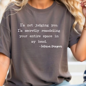 K&ouml;nnte beinhalten: Ein graues T-Shirt mit dem Text "Ich verurteile dich nicht. Ich renoviere heimlich deinen gesamten Raum in meinem Kopf. - Innenarchitekt" in wei&szlig; gedruckt.