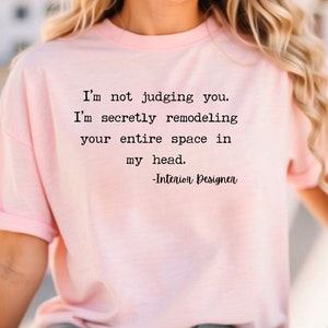 K&ouml;nnte beinhalten: Ein pinkfarbenes T-Shirt mit einem lustigen Zitat &uuml;ber Innenarchitektur. Der Text lautet: "Ich beurteile dich nicht. Ich renoviere heimlich deinen gesamten Raum in meinem Kopf. -Innenarchitekt"