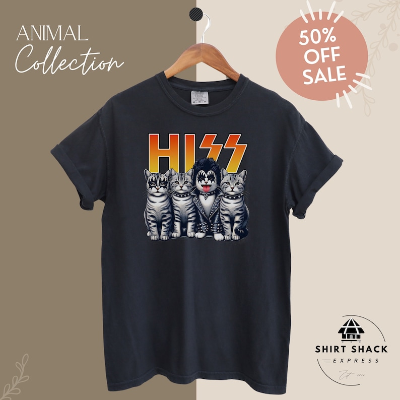 以下が含まれることがあります： KISSのバンドの衣装を着た4匹の猫のグラフィックがプリントされた黒いTシャツ。グラフィックには、赤、オレンジ、黄色のフォントで「HISS」と書かれています。